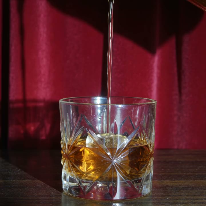 Whiskey pouring into a cut-crystal rocks glass in front of a red velvet curtain